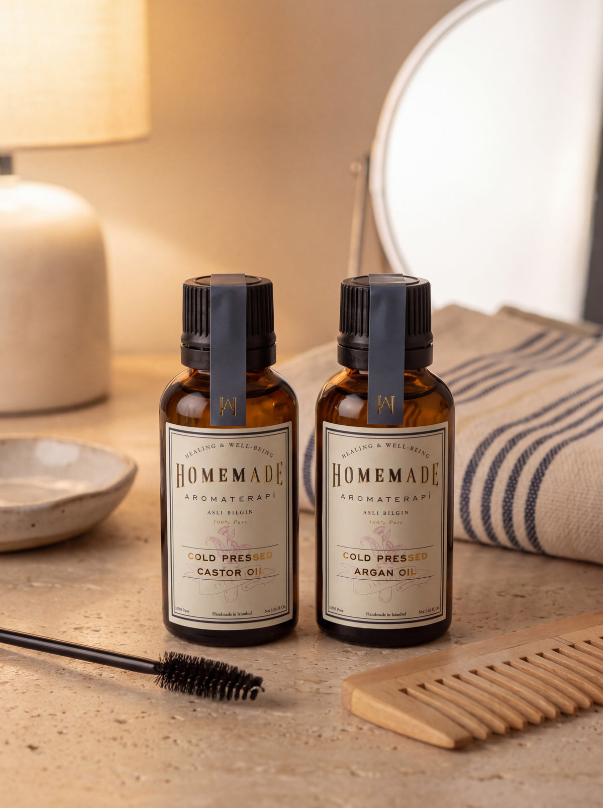 Two HomeMade Aromaterapi cold-pressed oils (Castor and Argan) displayed on a bathroom vanity with grooming tools and mirror.