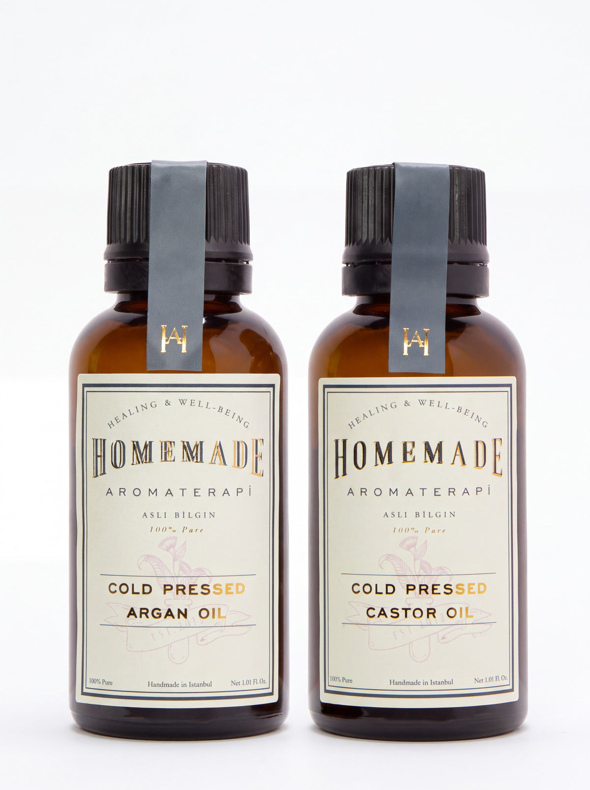 Two Homemade Aromaterapi cold-pressed oils—Argan Oil and Castor Oil—in amber glass bottles with gray ribbon labels on a clean white background.