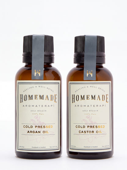 Two Homemade Aromaterapi cold-pressed oils—Argan Oil and Castor Oil—in amber glass bottles with gray ribbon labels on a clean white background.